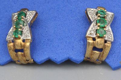 une paire de boucles d'oreilles en émeraude et diamant posées sur un tissu bleu