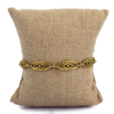 un bracelet plaqué or posé sur un coussin, sur un fond blanc