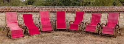 several pink lawn chairs are lined up in a row in a field
