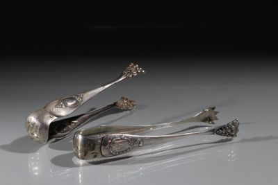 deux cuillères en argent et une pince posées sur une surface blanche