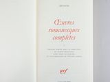 an open book on a table with a white cover and red lettering
