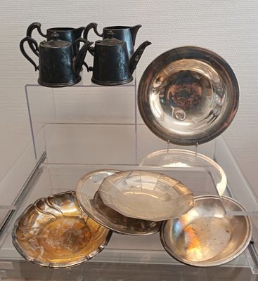 une vitrine en verre dans laquelle sont exposés des assiettes et des tasses en argent