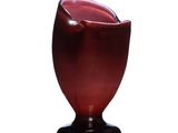 un vase rouge avec un socle noir posé sur une surface blanche
