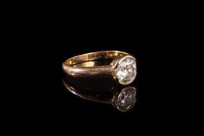 un gros plan d'une bague en or sertie d'un diamant, posée sur une surface noire