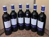 six bottles of red wine are lined up on a barrel