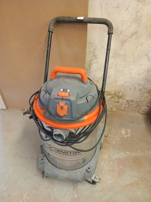 un aspirateur orange et gris posé sur le sol, près d'un mur