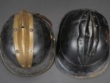 two helmets with gold stripes on them sitting on a gray surface