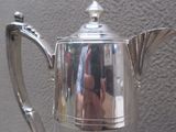 une cafetière en argent posée sur une table près d'un mur