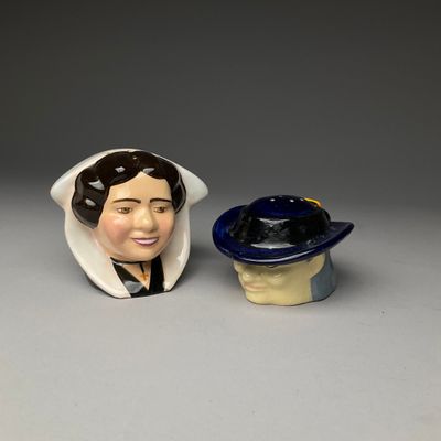 two ceramic figurines of a woman and a hat on a table