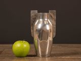 a silver vase with a green apple next to it