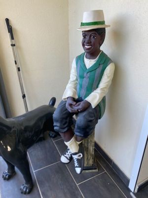 a statue of a man sitting on a stool next to a black dog