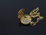 a gold pocket watch with a chain on a black surface