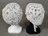 deux bonnets en dentelle blanche posés sur un support noir, sur fond gris