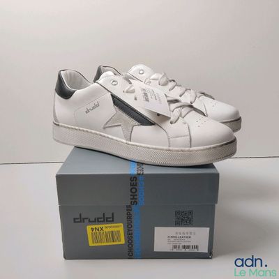 une paire de baskets blanches posée sur une boîte, elle-même posée sur une table