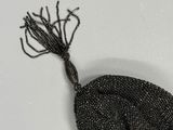 un vieux sac noir orné de perles et d'un pompon, sur un fond blanc