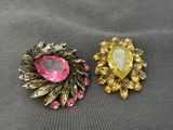 two brooches with pink and yellow stones on them