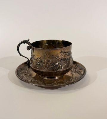 une tasse et une soucoupe anciennes en argent, posées sur une soucoupe