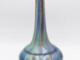 un vase rayé de bleu et de vert posé sur une surface blanche