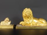 une paire de statues de lions en or posées sur des socles en marbre, sur un fond noir