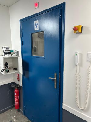 une porte bleue dans une pièce où se trouve un téléphone accroché au mur