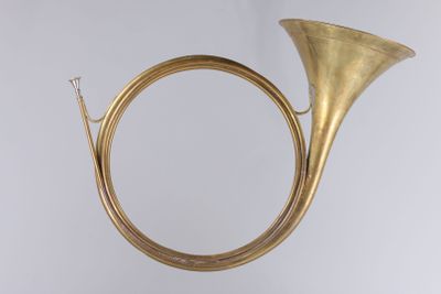 an antique brass french horn on a stand against a white background
