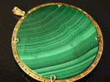 an image of a close up of a green and gold pendant on a black surface