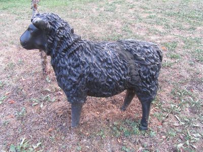 une statue représentant un mouton noir debout dans l'herbe