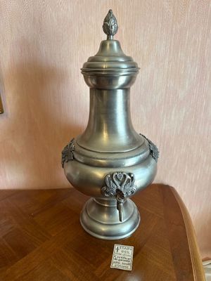 a silver vase sitting on a wooden table with a lamp on it