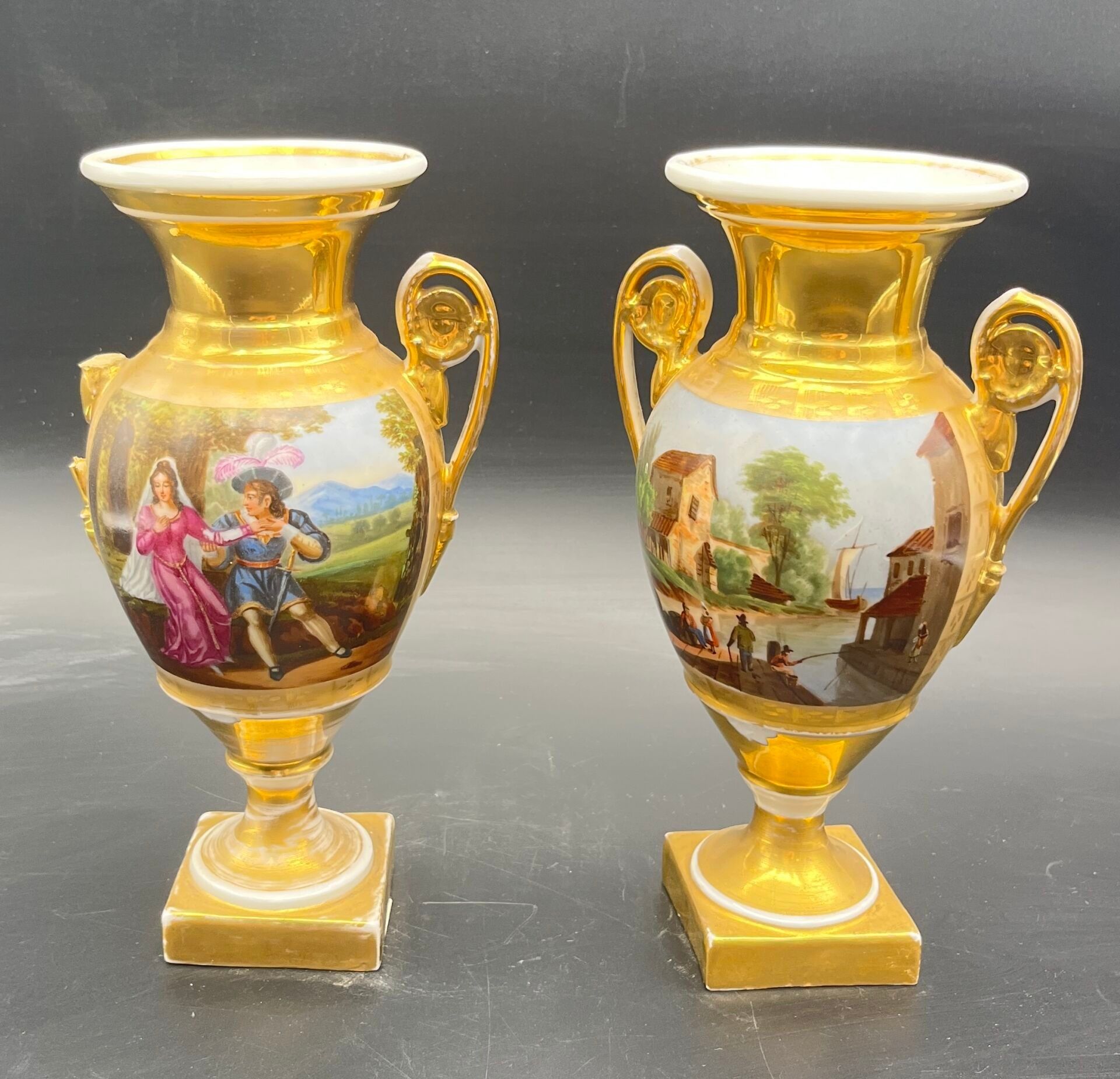 Paire de vases Médicis en porcelaine peinte à décor de scènes galantes. H 25 cm. (égrenures, une anse cassée, rayures)