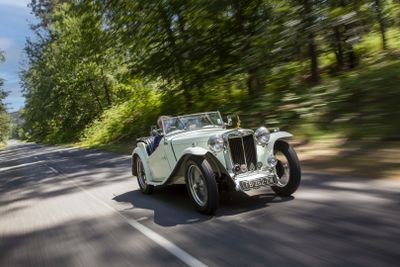 a white vintage car driving down the road in the woods