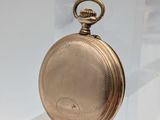 une montre de poche en or exposée sur un socle transparent