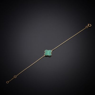 a gold bracelet with a green clover charm on a black background