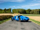 a blue race car driving down the road in the middle of a field
