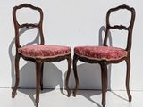 two wooden chairs with red upholstered cushions against a white wall