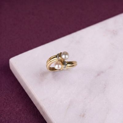 bague en perle et diamant posée sur une plaque de marbre, sur fond violet