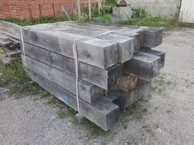 Plusieurs morceaux de bois sont empilés les uns sur les autres devant un bâtiment en briques