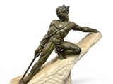 statue of a man sitting on a rock holding a spear