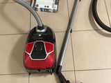 un aspirateur posé par terre à côté d'un carton contenant des bouteilles de vin