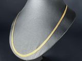 un collier en or posé sur un mannequin noir, devant un fond noir
