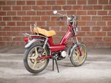 a small red motorcycle parked in front of a brick wall