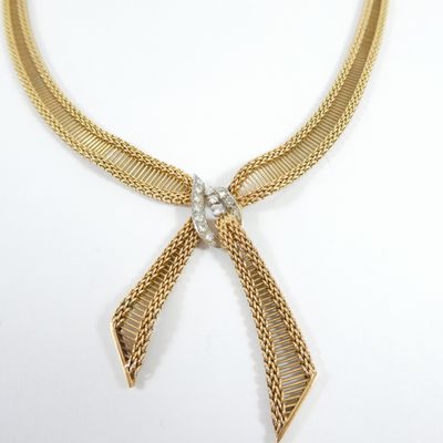a close up of a gold necklace with a bow on a white background