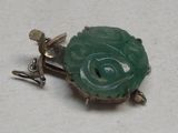 une photo d'une broche en forme de tortue en jade vert posée sur une surface blanche