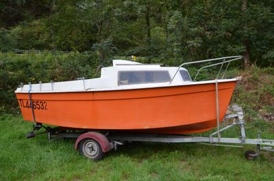 un petit bateau orange sur une remorque, dans l'herbe