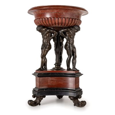 un grand socle en bronze et en marbre rouge surmonté de deux hommes tenant un bol