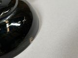 a black vase with a wooden handle on a white table