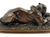 bronze statue of a dog laying down on the ground with a hat on its head