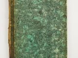 an old book with a green cover sitting on top of a white surface