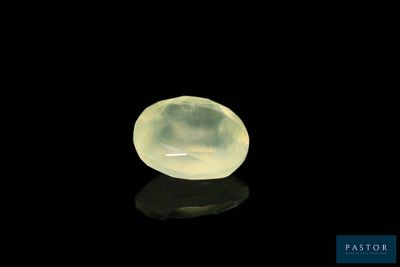 une pierre de jade jaune posée sur une surface noire, avec un reflet