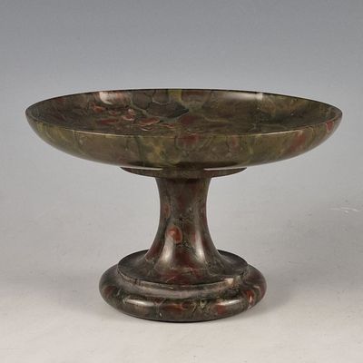 un bol ancien en bronze posé sur un socle, sur une surface blanche