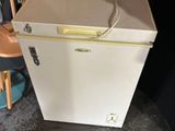 a small white refrigerator with a red top and a wooden chair